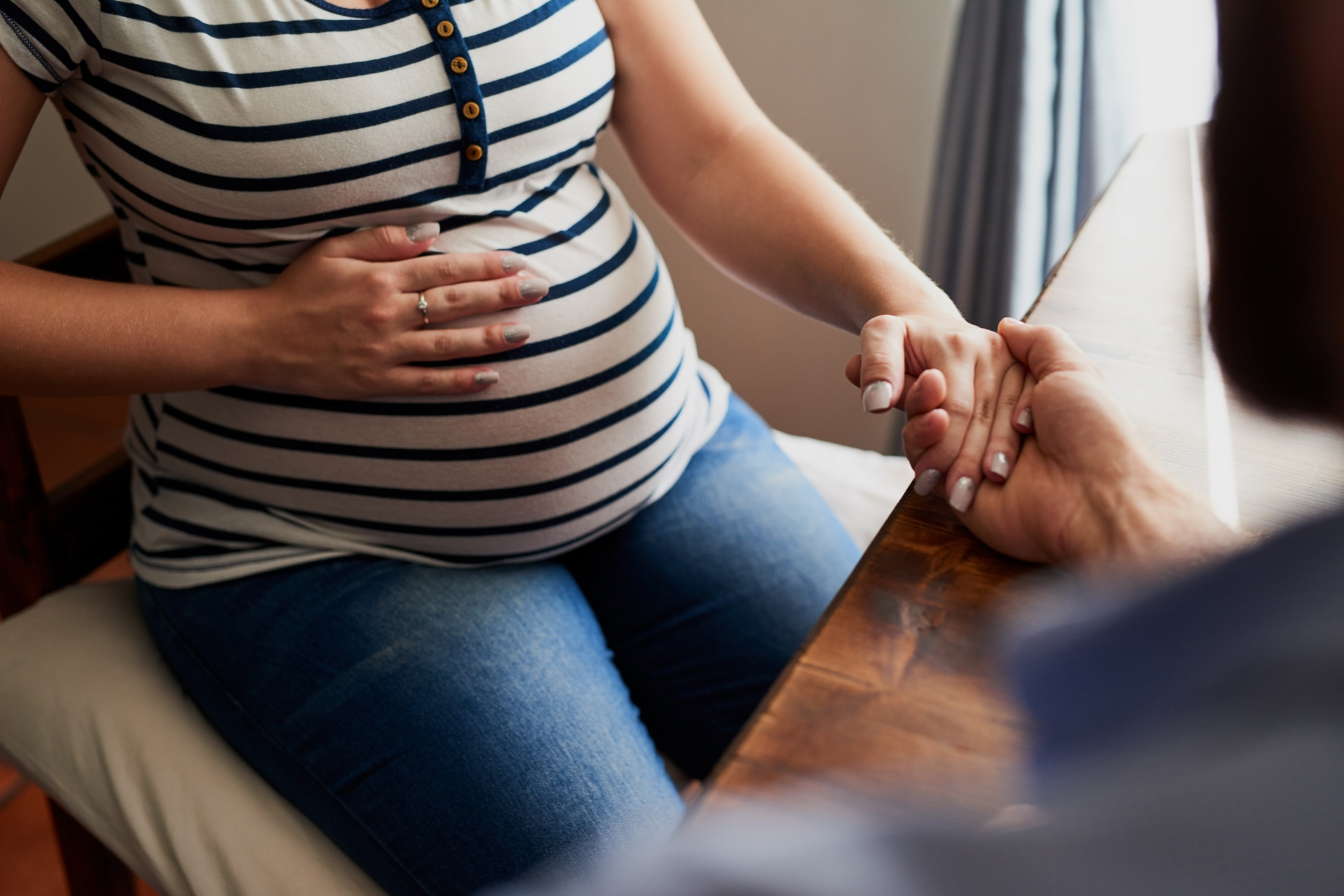 A clinician holding a pregnant patient's hand during a visit